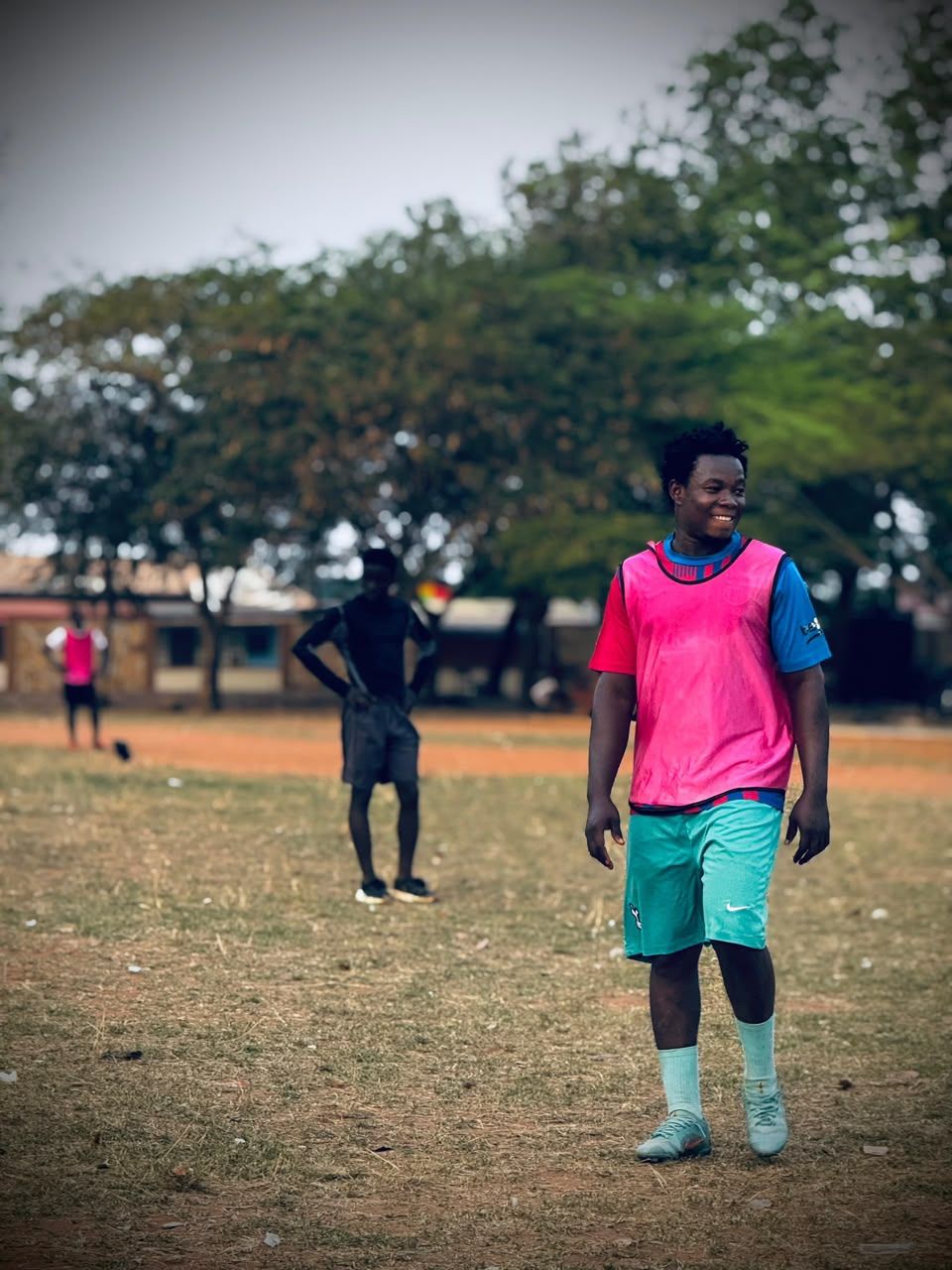 A smiling player in a pink training bib on the pitch
